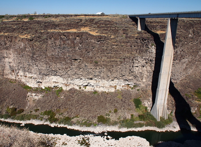 [One short bridge strut rests on a step of the canyon wall while the next one goes all the way down to the river level. The car on the bridge is a small speck on the bridge deck.]